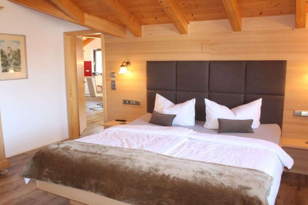 Un dormitorio con una cama grande, cabecera, lámparas de noche y techo de madera.