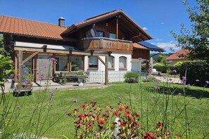 A two-story house with a balcony, a garden with flowers, and a clear blue sky. - Holiday apartment with 2 bedrooms (Oberstaufen \/ Allgäu)