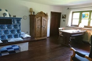A room with a wooden cabinet, a dining table with chairs, a window with curtains, and a radiator. - Holiday home on Lake Chiemsee (Breitbrunn am Chiemsee)
