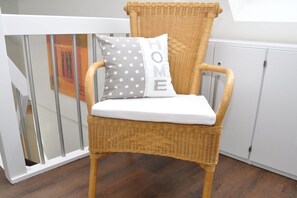 A wicker chair with a white cushion and two pillows, one with stars and the other with the word 'HOME' on a white background. - Holiday apartment with 1 bedroom (Krummhörn \/OT Greetsiel)