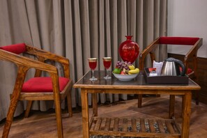 Uma mesa de madeira com uma tigela de frutas, dois copos e um vaso vermelho.
