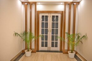 A hallway with a double door, potted plants, and a tiled floor. - Hotel Royal Park (Budgam)