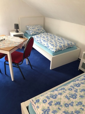 A small, single-bed room with a desk and chair, a nightstand, and a lamp.