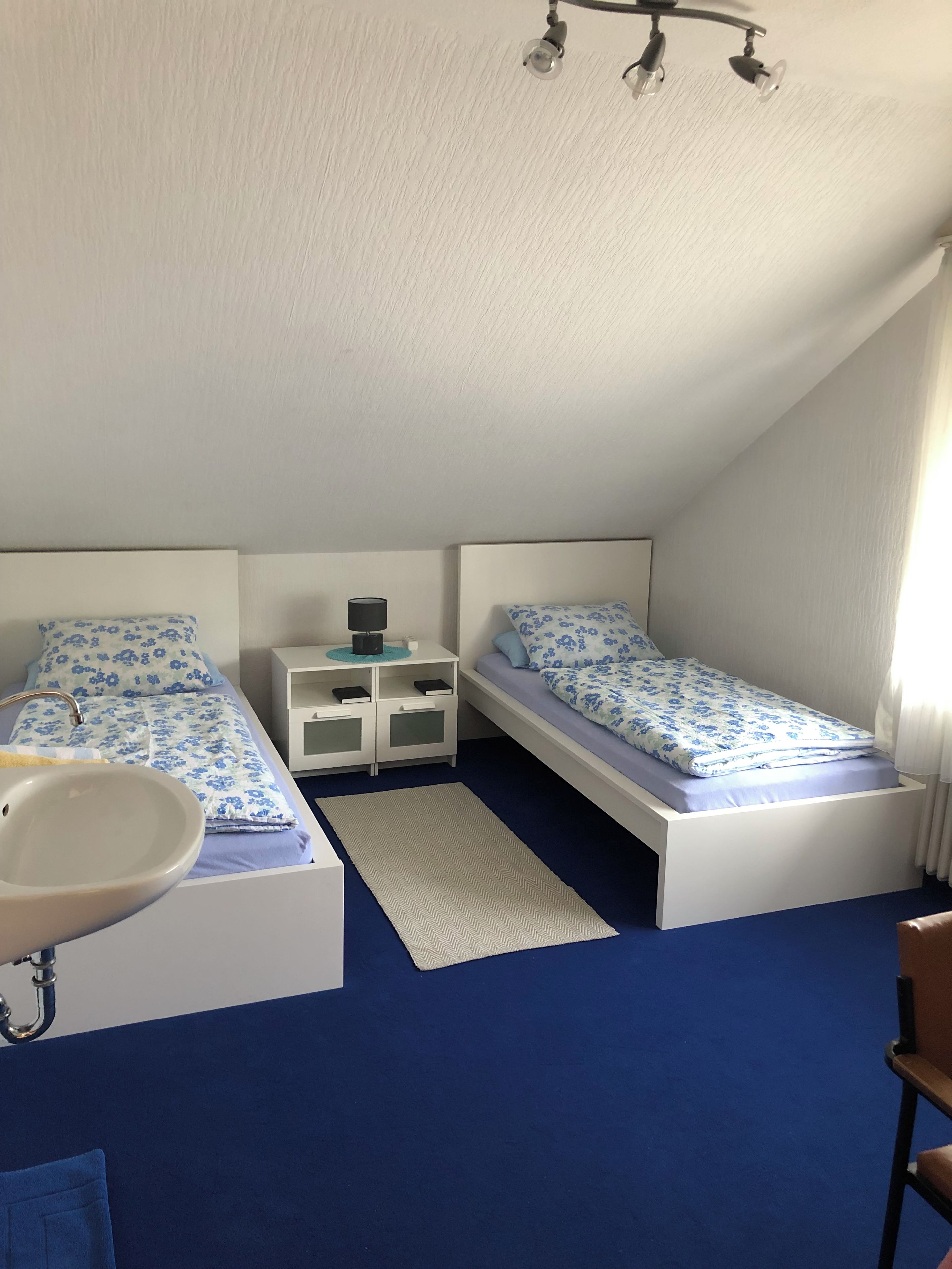 Ein Schlafzimmer mit zwei Betten, einem Nachttisch, einem Schminktisch, einem Fenster und einem Badezimmer mit Waschbecken.