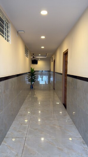 Un pasillo con piso de baldosas, luces empotradas en el techo, una planta en maceta y una puerta a la derecha.