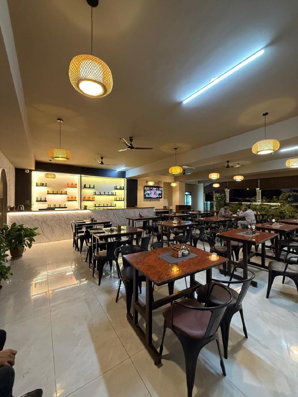 A restaurant with multiple tables and chairs, ceiling fans, and hanging lamps.