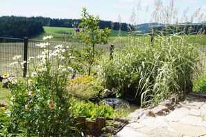 A garden with a variety of plants, a stone pathway, and a view of a green field beyond a fence. - Holiday apartment with 1 bedroom (St. Märgen)