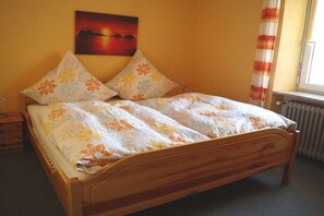 A single bed with floral bedding, a nightstand, a wall-mounted painting, and a window with curtains. - Holiday apartment with 1 bedroom (St. Märgen)