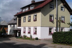Ein zweistöckiges Gebäude mit rotem Dach, zahlreichen Fenstern und Blumenkästen im Erdgeschoss.