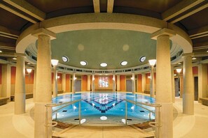 Ein großes Hallenbad mit einer zentralen Treppe, umgeben von Säulen und einer hohen Decke.