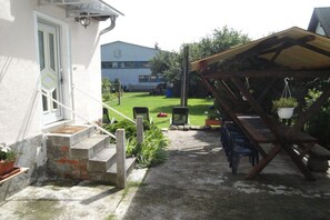 Ein überdachter Außenbereich mit Tisch und Stühlen, einer Holzw pergola und einer Treppe zum Hauseingang.