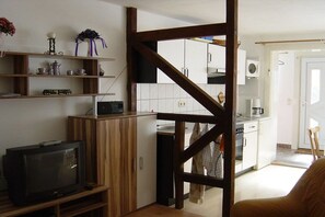 Ein kompakter Wohnbereich mit Küchenzeile, Fernseher und einer Holztreppe.