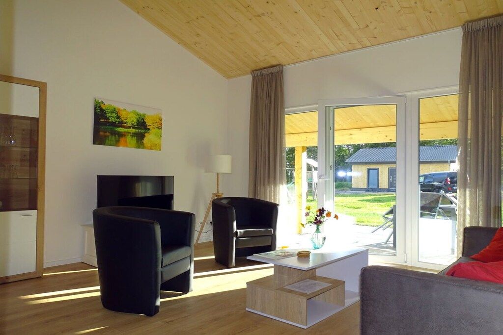 Ein modernes Wohnzimmer mit einem Flachbildfernseher, zwei schwarzen Sesseln, einem grauen Sofa, einem Couchtisch und einem Gemälde eines Sees.