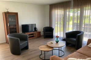 Un saló modern amb televisió plana, dos seients còmodes, un sofà i una taula de centre.