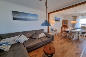Ein Wohnzimmer mit einer Couch, einem runden Couchtisch und einem Essbereich mit Tisch und Stühlen.