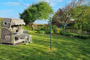 A garden with a wicker chair and a small table, surrounded by a wooden fence and greenery. - North Sea house with pirate's nest (Nordstrand)