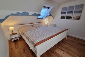 Une chambre avec un plafond en pente, un lit doté d’une tête de lit en bois, une table de chevet avec une lampe et une étagère fixée au mur.