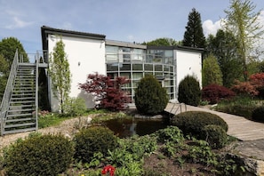 Ein modernes Gebäude mit Glasfassade, einer Holzterrasse und einem kleinen Teich im Garten.