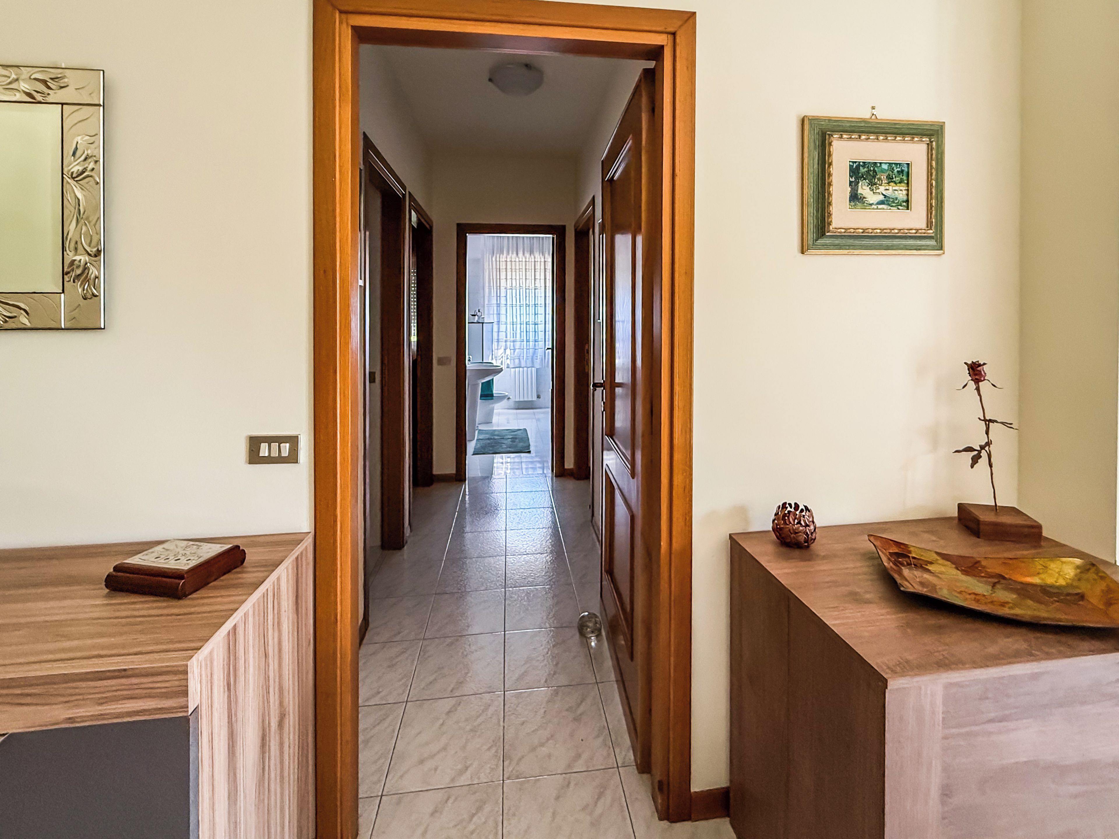 Un corridoio con porte in legno che dà accesso a un bagno e a una zona living.