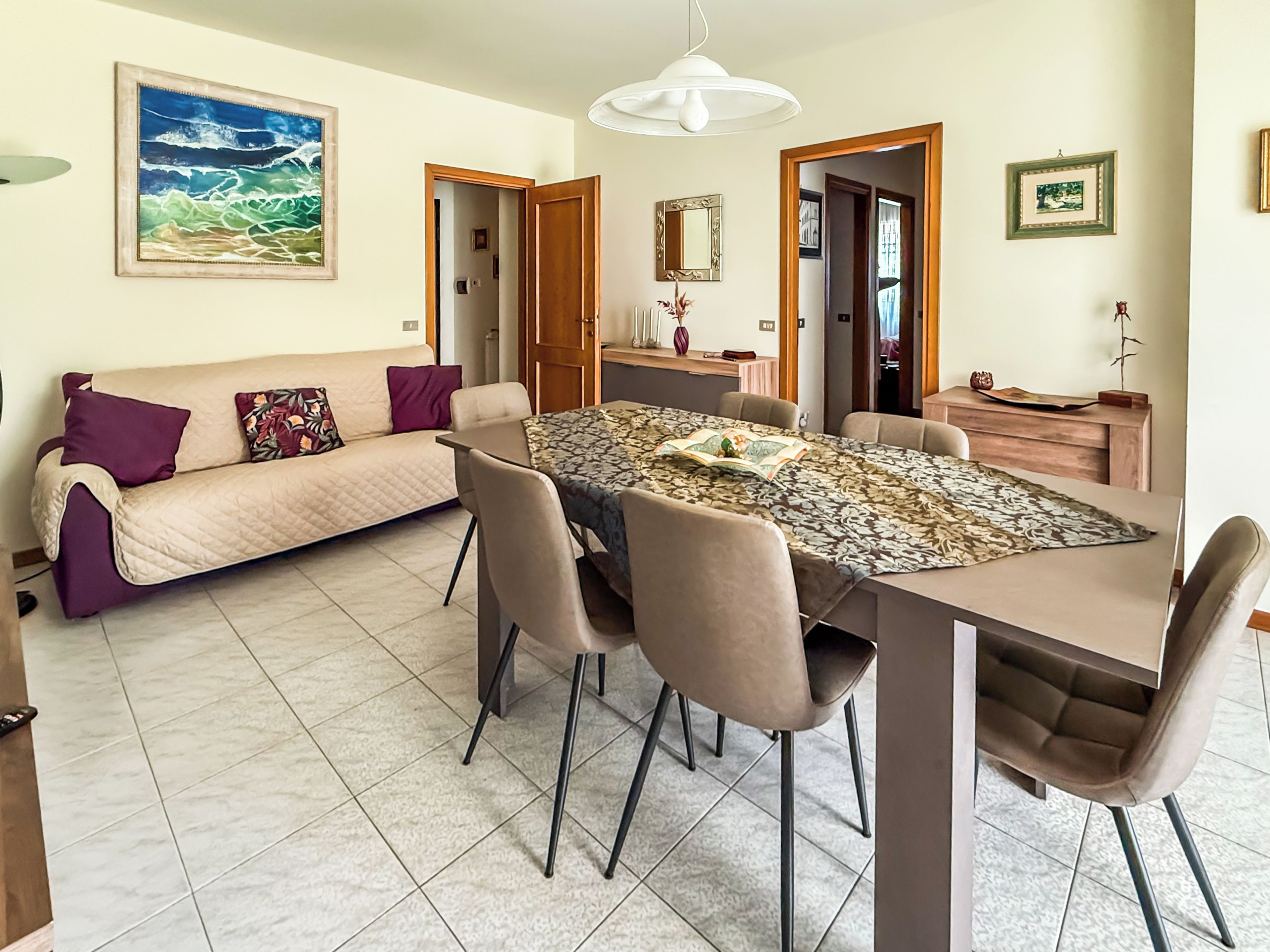 A dining area with a table, chairs, a sofa, and a painting on the wall.