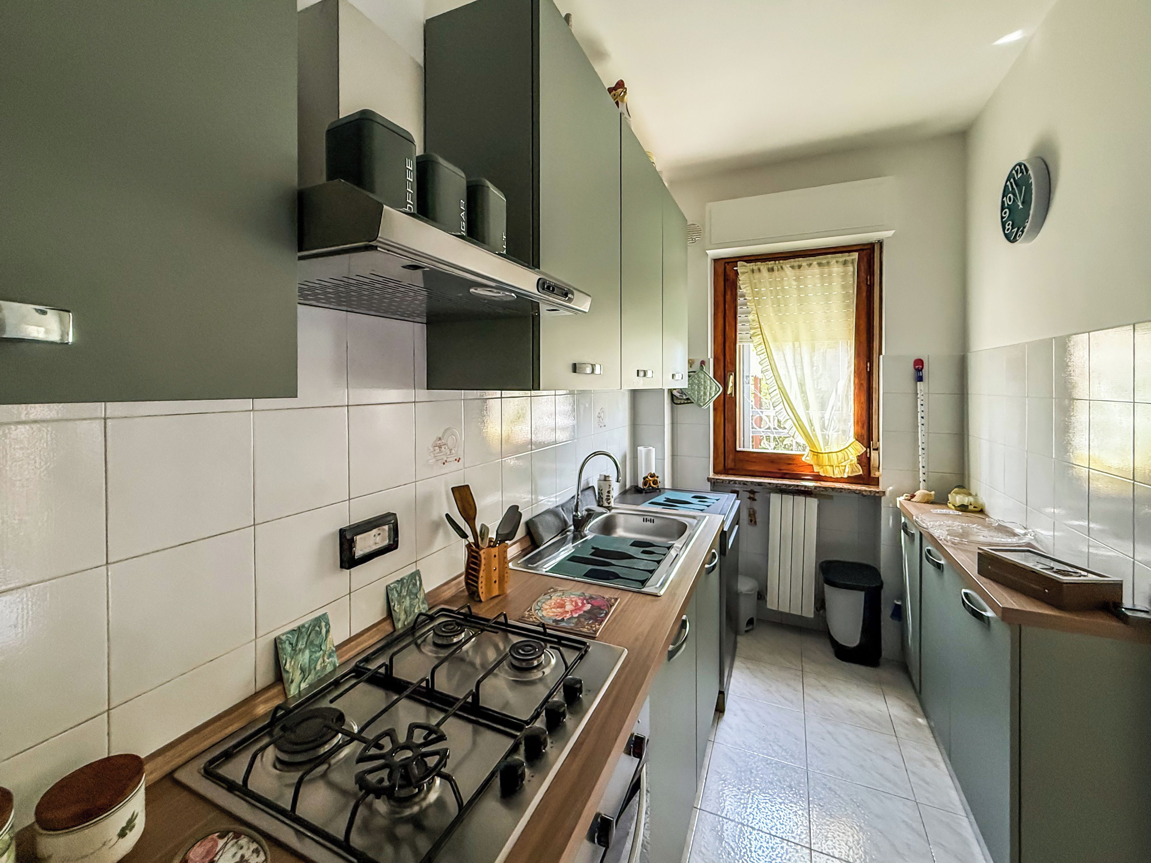 A compact kitchen with a gas stove, a sink, and a window with curtains.