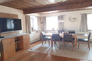 Ein Essbereich mit einem Holztisch und Stühlen, einem Fernseher auf einem Holzschrank und einem Kruzifix an der Wand.