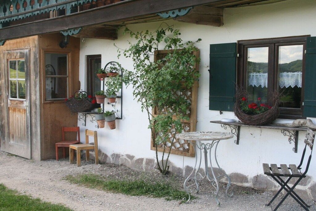 A rustic building with a wooden door, a small table, and a chair outside.
