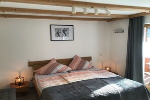 Quarto com cama, mesa de cabeceira, luminária na parede, quadro emoldurado e janela com cortinas.