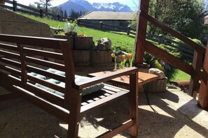 A wooden bench with cushions, a small table, and a stone ledge with flowers and a vase. - Holiday apartment with 1 bedroom (Bischofswiesen)
