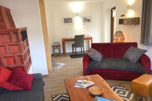 Ein Wohnzimmer mit einem roten Sofa, einem Holztisch und einem roten Sessel. Im Hintergrund steht ein kleiner Schreibtisch mit einem Stuhl.