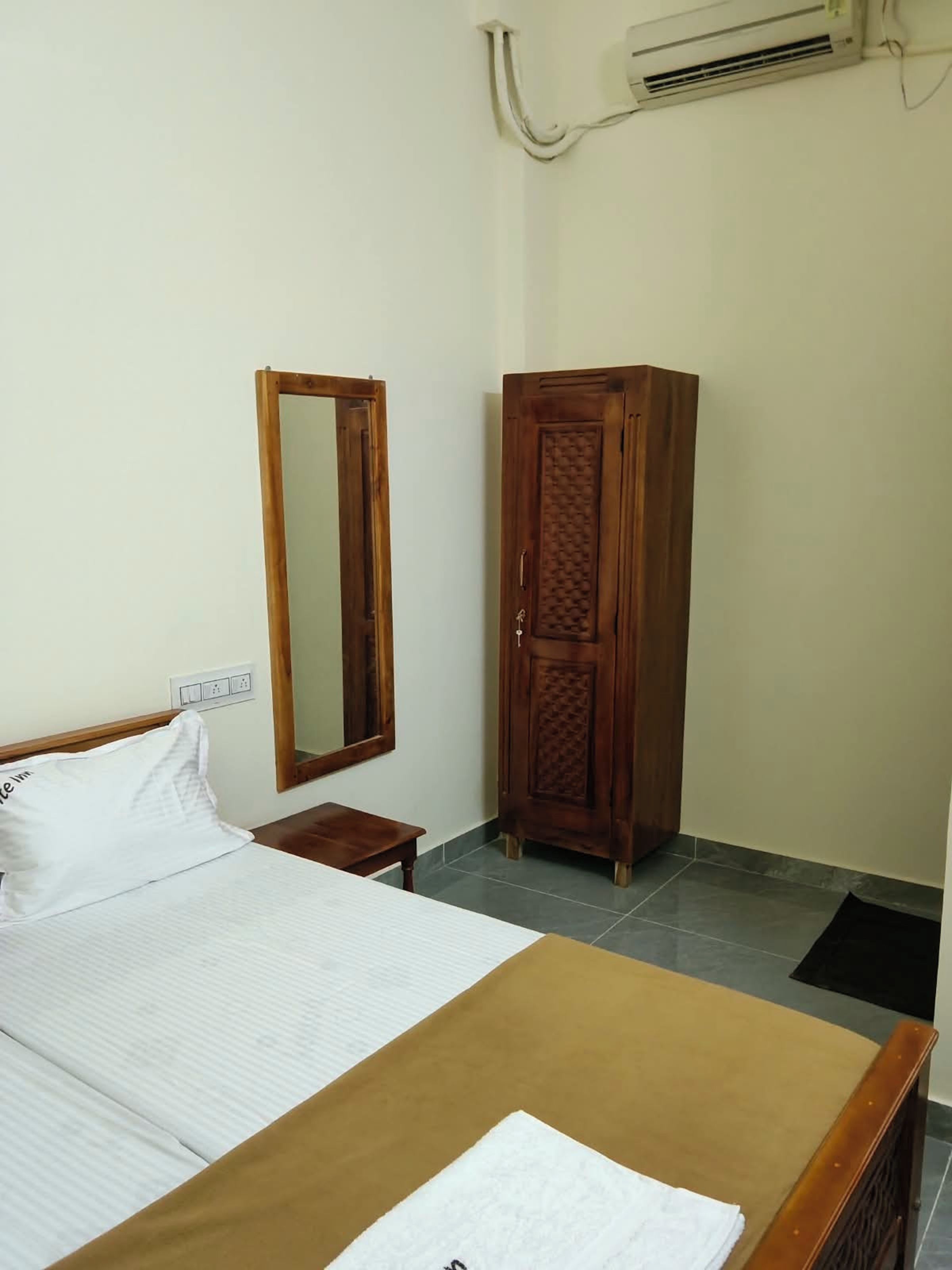 Una habitación de hotel con una cama, un armario, un espejo y un aire acondicionado.