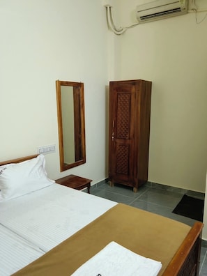 A hotel room with a bed, a wardrobe, a mirror, and an air conditioning unit.