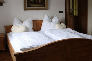A wooden bed with white bedding and pillows, a wooden headboard, a nightstand, a painting on the wall, and a door with a glass panel. - Holiday apartment with 2 bedrooms (Bischofswiesen)