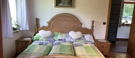 Ein Bett mit Holz-Kopfteil, einer grün-weißen Karomatte und herzförmigen Kissen.