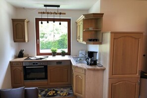 A compact kitchen with wooden cabinets, a built-in oven, a coffee maker, and a window with a view of greenery. - Holiday apartment with 2 bedrooms (Bischofswiesen)