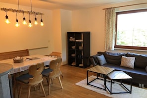 A living room with a sofa, a dining table with chairs, a bookshelf, and a window with curtains. - Holiday apartment with 2 bedrooms (Bischofswiesen)