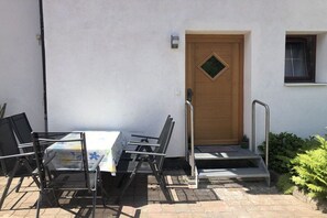 An outdoor patio with a table and chairs, a wooden door, and a small window. - Holiday apartment with 2 bedrooms (Bischofswiesen)