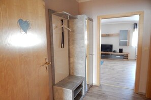 Une pièce avec une porte en bois, un banc, un porte-serviettes et un téléviseur à l’arrière-plan.