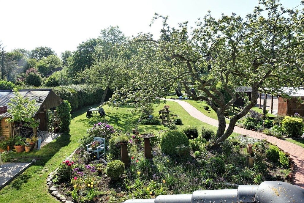 Een verzorgde tuin met verschillende planten en een gazon, een pad en een gebouw met een schuin dak.