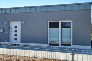Ein modernes Gebäude mit einer grauen Fassade, einer weißen Tür und einem großen Fenster mit einem Metalleinschlag.