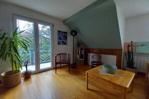 A living room with a wooden floor, a dining table, a potted plant, a bookshelf, and a large window. - Holiday apartment with panoramic views (Weinheim)