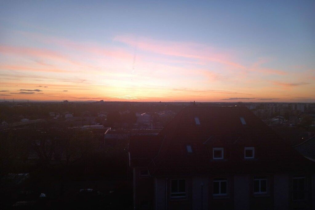 Solnedgang over et bybillede med silhuetter af bygninger mod himlen.