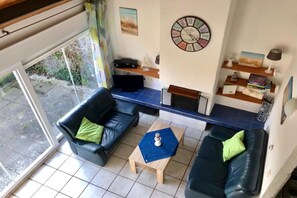 A living room with two black leather sofas, a wooden coffee table, a wall clock, and a bookshelf. - Holiday home with 1 bedroom (Bruinisse)