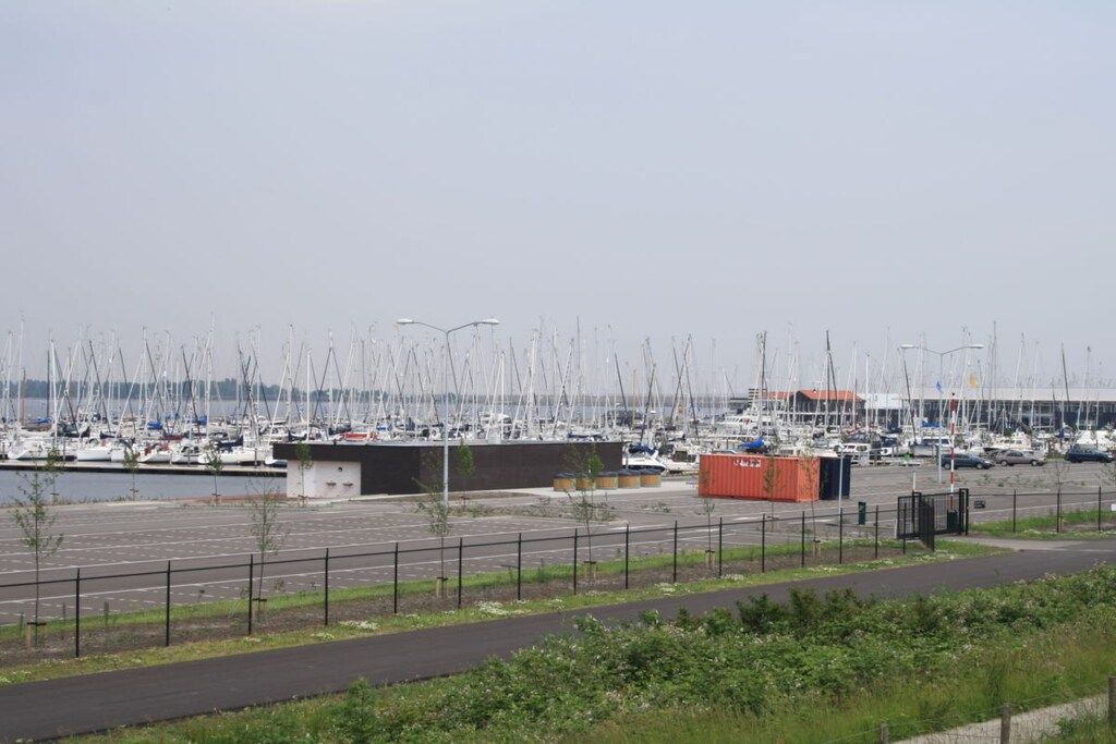 A marina with numerous sailboats docked, a parking area, and a small building.