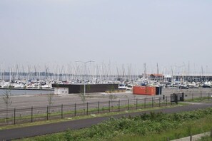 Een jachthaven met veel zeilboten afgemeerd, een parkeerplaats en een klein gebouw.