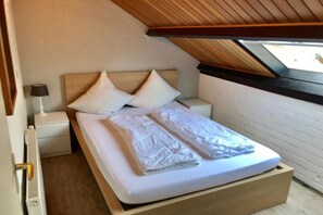 A single bed with a wooden headboard, white bedding, and a nightstand with a lamp. - Holiday home with 1 bedroom (Bruinisse)