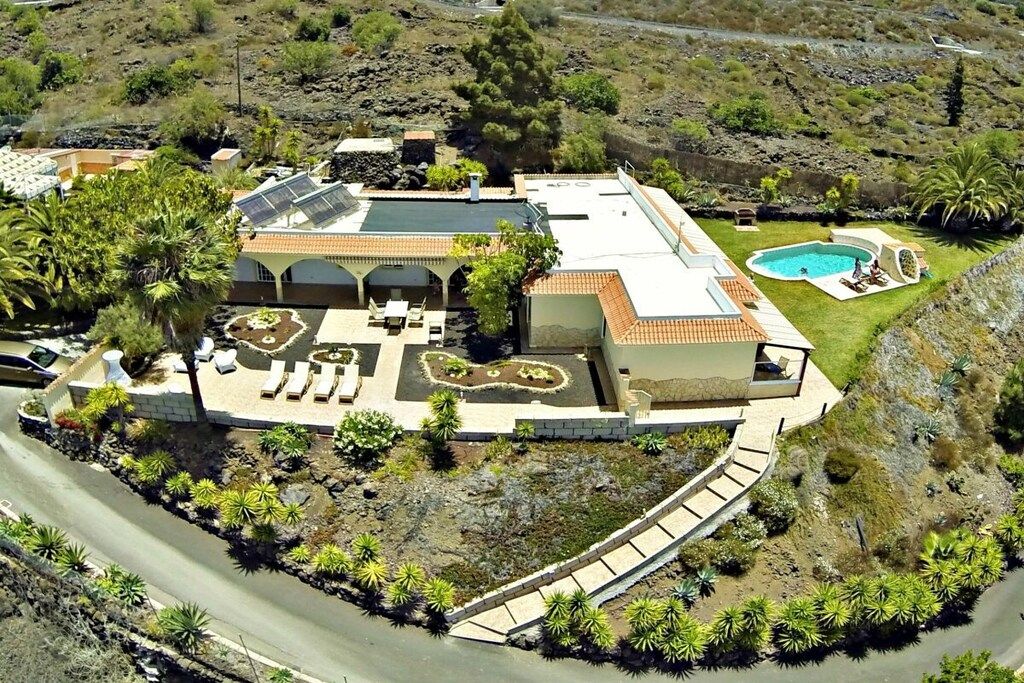 Ein modernes Haus mit Swimmingpool, einer Terrasse mit Sitzgelegenheit und einem angelegten Garten.
