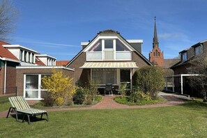 Un immeuble résidentiel doté d’un toit en pente, d’une cheminée visible et d’un petit jardin avec une pelouse et une chaise.