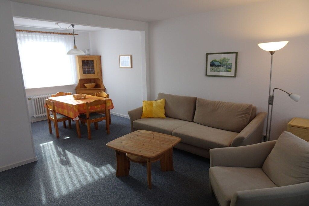 Ein Wohnzimmer mit einer Couch, einem Couchtisch, einem Esstisch mit Stühlen, einer Lampe und einer Heizung.