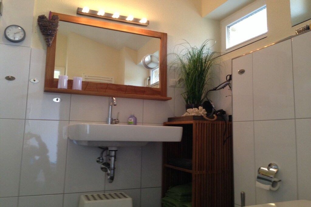 Un baño con tocador, lavamanos, espejo y una pequeña ventana.